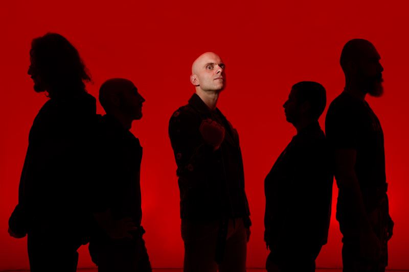 Band portrait: five musicians backlit against a red backdrop