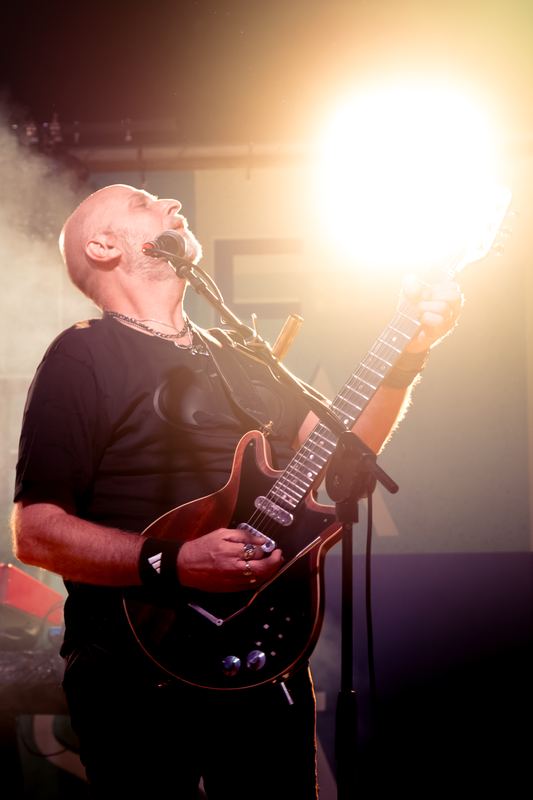 Guitarist singing with his head back, backlit by stage lights
