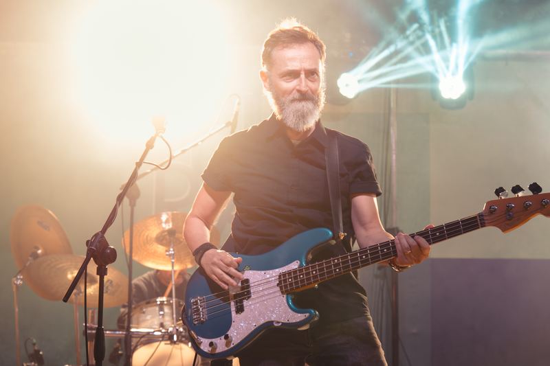 Smiling bassist on stage with a blue bass and light beams behind him