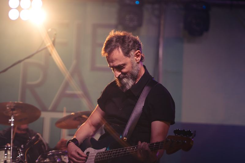 Bassist focused on stage in warm light, drum kit behind him