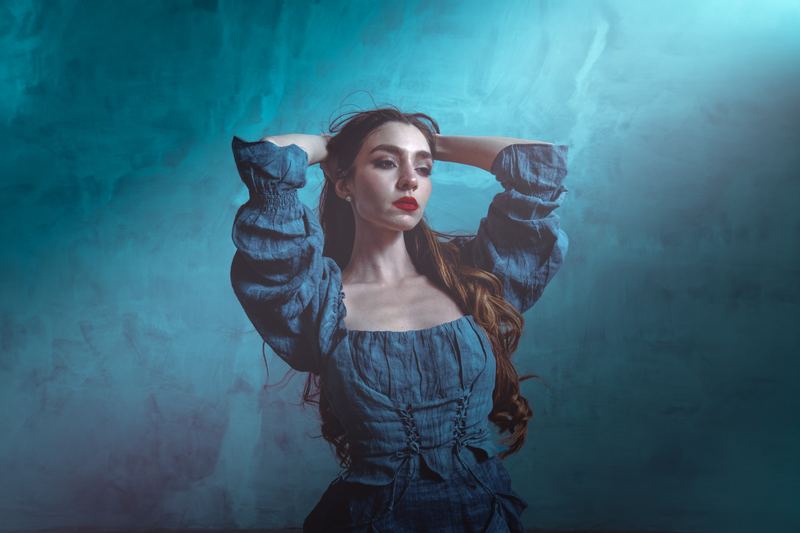 Ritratto di moda: braccia alzate tra i capelli, denim su fondale verde acqua