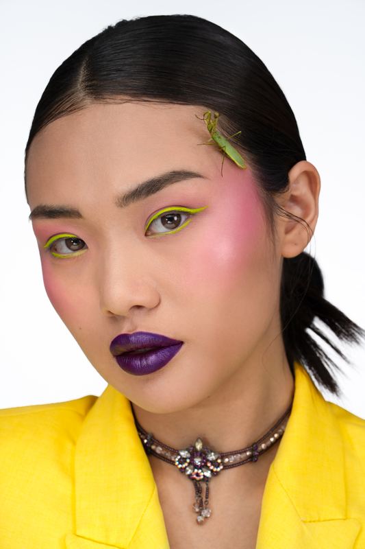 Ritratto beauty: eyeliner giallo, labbra viola, mantide sui capelli, giacca gialla