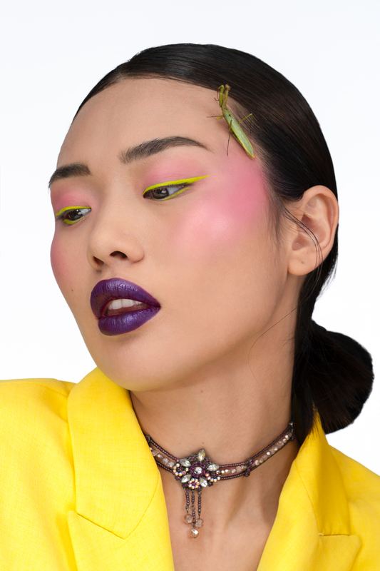 Ritratto beauty di profilo: labbra viola, guance rosa e una mantide verde tra i capelli
